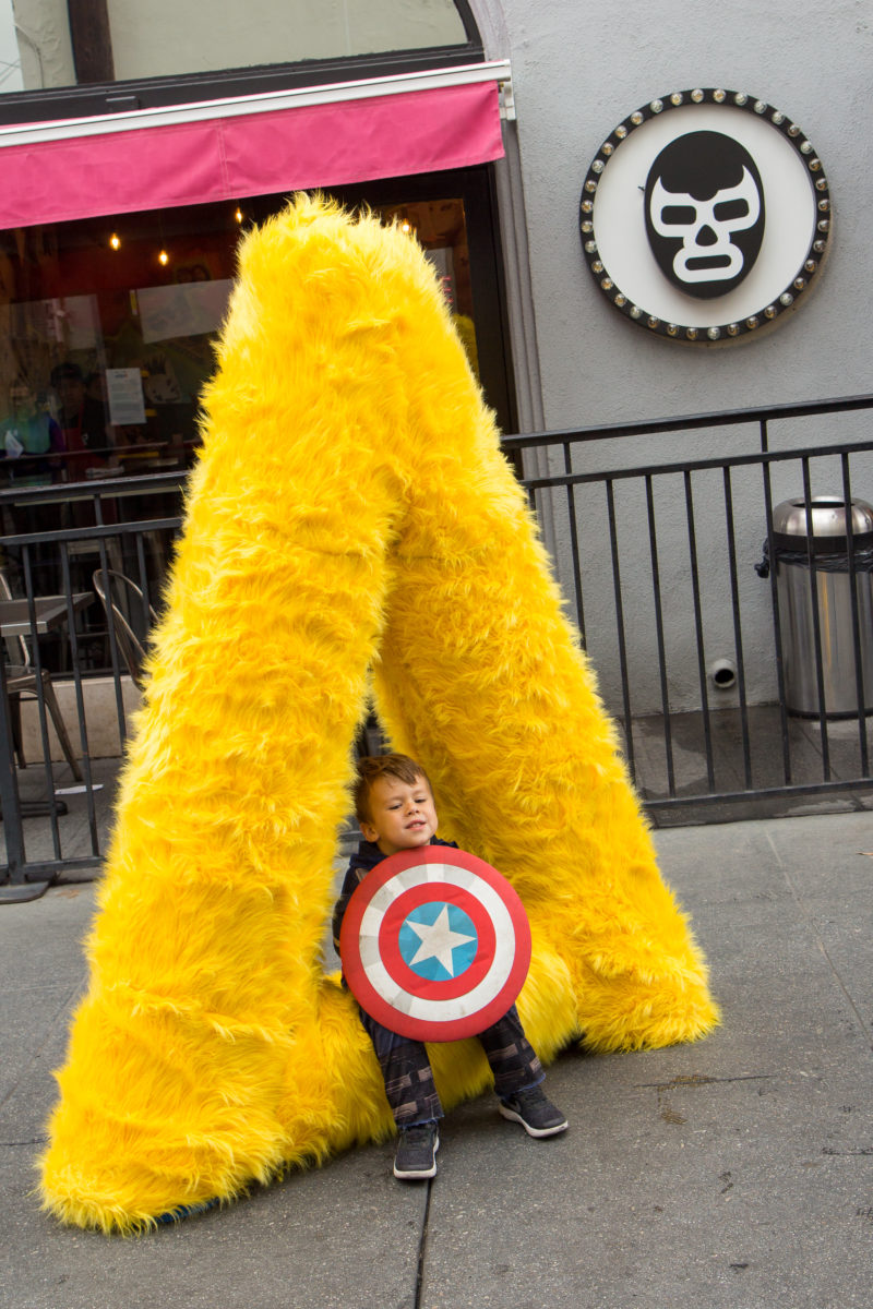 a boy with a captain america shield sitting on a yellow fur triangle sculpture